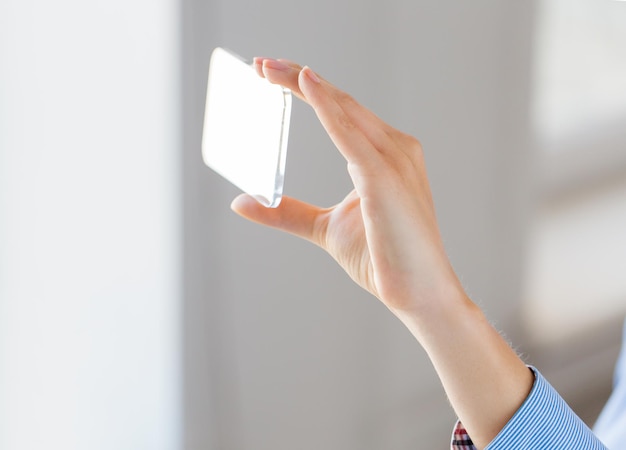Geschäfts-, Technologie- und Personenkonzept - Nahaufnahme einer Frau, die ein transparentes Smartphone im Büro hält und zeigt