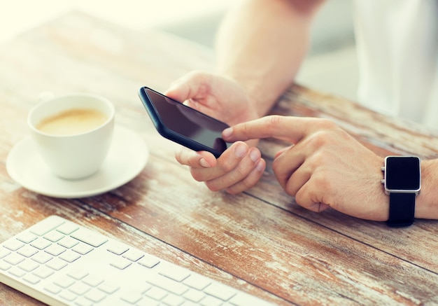 Geschäfts-, Technologie- und Personenkonzept - Nahaufnahme einer männlichen Hand, die ein Smartphone hält und eine Uhr mit Kaffee und Tastatur am Holztisch trägt