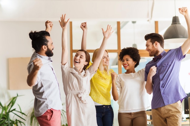 Geschäfts-, Triumph-, Gesten-, Menschen- und Teamwork-Konzept - fröhliches internationales Kreativteam, das die Hände hochhebt und den Sieg im Amt feiert