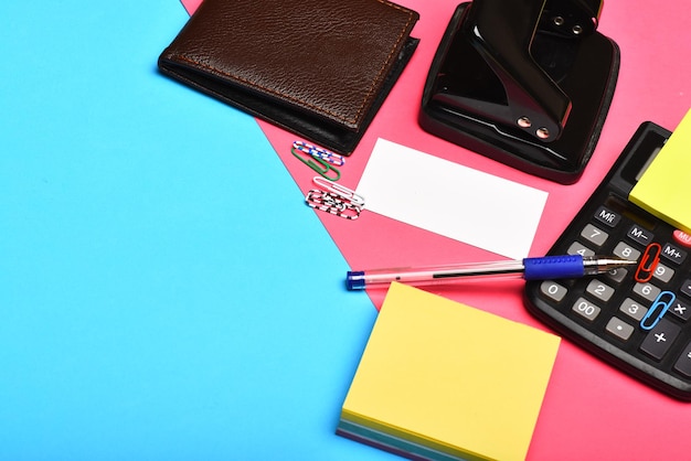Geschäfts- und Arbeitskonzept Mans Ledergeldbörse und Schreibwaren kopieren Platz Taschenrechner Lochkarte Notizpapier Stift und Clips Bürowerkzeuge isoliert auf rosa und blauem Hintergrund Nahaufnahme