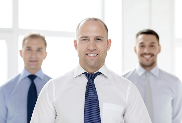 Geschäfts- und Bürokonzept - lächelnder Geschäftsmann im Büro mit Team auf dem Rücken