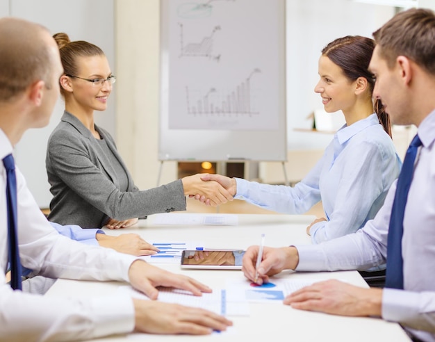 Geschäfts- und Bürokonzept - zwei lächelnde Geschäftsfrauen, die sich im Büro die Hände schütteln