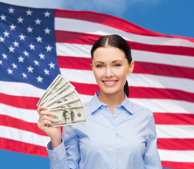 Geschäfts- und Geldkonzept - junge Geschäftsfrau mit Dollarbargeld über Hintergrund der amerikanischen Flagge