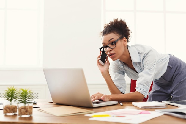 Geschäftsanruf tätigen. Ernsthafte CEO-Geschäftsfrau, die im modernen Büro auf dem Handy spricht und am Laptop arbeitet, Platz kopieren