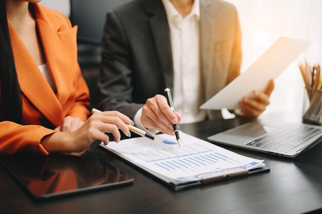 Geschäftsdokumente auf dem Bürotisch mit Smartphone und Taschenrechner, digitalem Tablet und Diagrammgeschäft mit Diagramm eines sozialen Netzwerks und zwei Kollegen, die Daten bei der Arbeit im Büro diskutieren