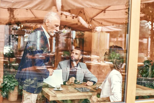 Geschäftsessen drei Leute im Restaurant sitzen am Tisch und diskutieren über das Projekt vor dem Fenster