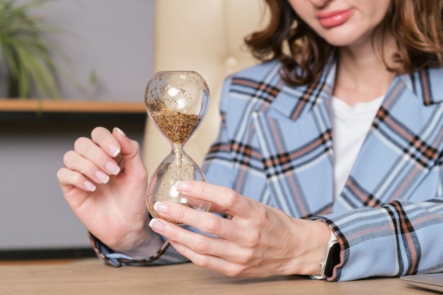 Geschäftsfrau an einem Schreibtisch hält Sanduhr mit glänzendem Sand in ihren Händen