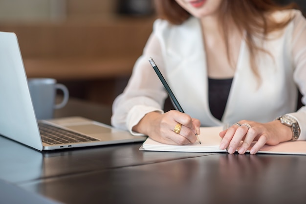 Geschäftsfrau, die am Laptop arbeitet und zur Kenntnis nimmt, während sie am Tisch im Büro sitzt