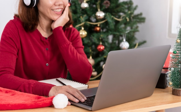 Geschäftsfrau, die am Weihnachtstag mit Geschenkbox und Weihnachtsbaumhintergrund am Computer arbeitet