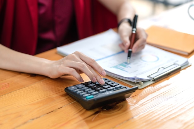 Geschäftsfrau, die an der Berechnung von Haushaltseinkommensstatistiken mit einem Taschenrechner arbeitet, der einen Stift hält, der auf die Grafik im Büro zeigt.