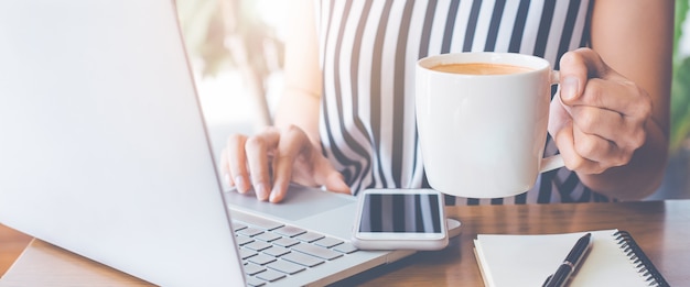 Geschäftsfrau, die an einem Laptop arbeitet und ihre Hand hält eine Tasse Kaffee.
