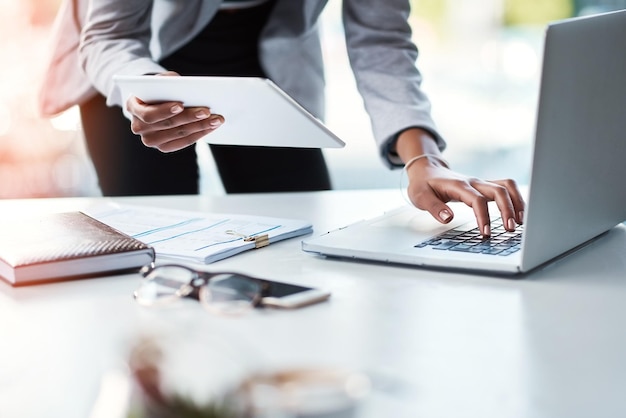 Geschäftsfrau, die an einem Laptop und Tablet arbeitet, eine Strategie plant und im Internet nach Projektideen sucht, während sie allein in einem Büro bei der Arbeit arbeitet Nahaufnahme der Hände eines Unternehmensleiters