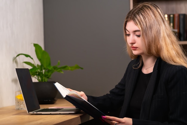 Geschäftsfrau, die an ihrem Schreibtisch im Büro aus einem Tagebuch liest, während sie ihren Zeitplan für den Tag in einer Nahansicht überprüft