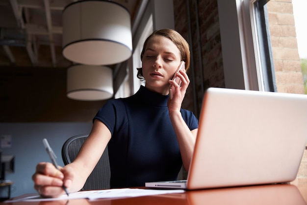 Geschäftsfrau, die an Laptop arbeitet und Telefonanruf tätigt