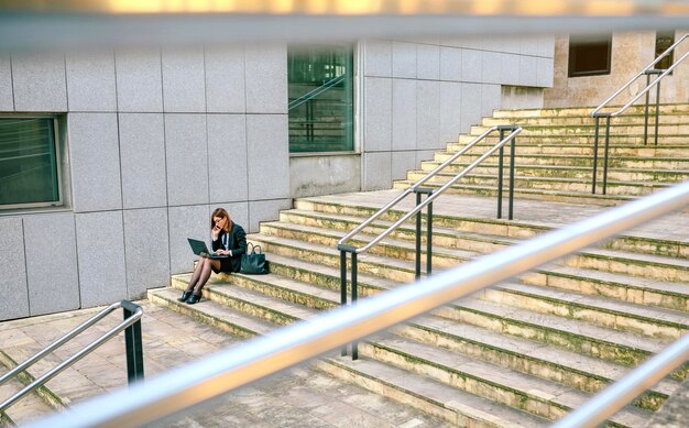 Geschäftsfrau, die auf Treppe sitzt und Laptop verwendet