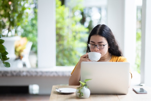 Geschäftsfrau, die beiläufig mit Laptop arbeitet und einen Kaffee hält