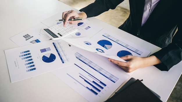 Geschäftsfrau, die beim Sitzen ein Taschenrechner-Analysediagramm von Finanzdaten am Schreibtischtisch verwendet