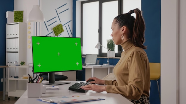 Geschäftsfrau, die Computer mit grünem Bildschirm im Startup-Büro verwendet. Firmenangestellter, der Monitor mit isoliertem Chroma-Key betrachtet und Kopierraumvorlage auf leerer Hintergrundanzeige nachahmt.