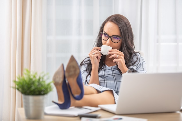 Geschäftsfrau, die die Füße hochlegt, Kaffee trinkt, eine Pause im Büro macht.
