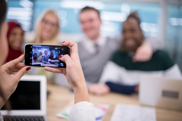 geschäftsfrau, die ein handy benutzt, um ihr multiethnisches geschäftsteam in einem modernen startbüro zu fotografieren