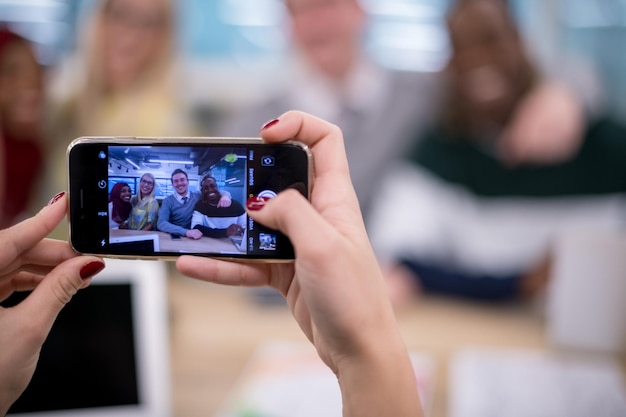 geschäftsfrau, die ein handy benutzt, um ihr multiethnisches geschäftsteam in einem modernen startbüro zu fotografieren