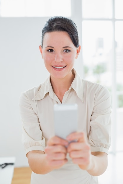 Geschäftsfrau, die ein Mobiltelefon im Büro hält