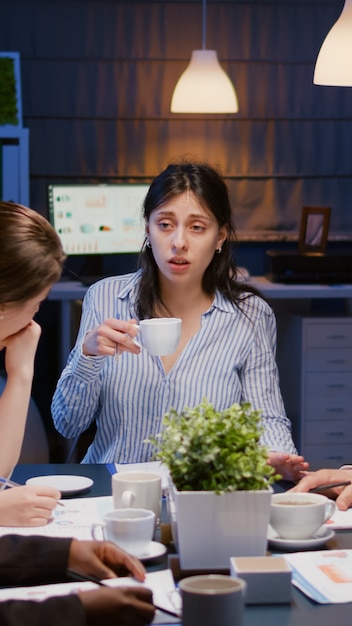 Geschäftsfrau, die eine Tasse Kaffee hält, während sie mit multiethnischer Teamarbeit diskutiert