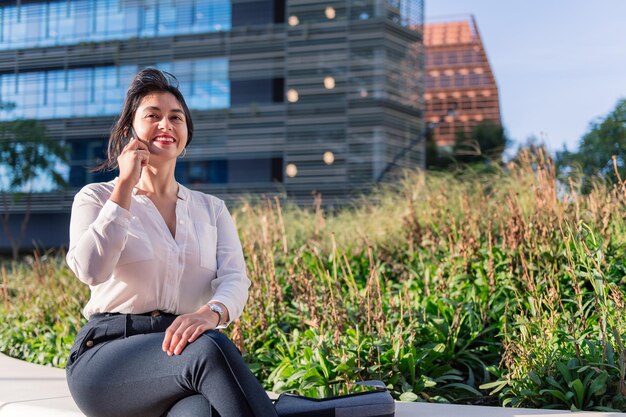 Geschäftsfrau, die in einem Park im Finanzviertel telefoniert, Konzept des Unternehmers und des urbanen Lebensstils, Platz für Text kopieren