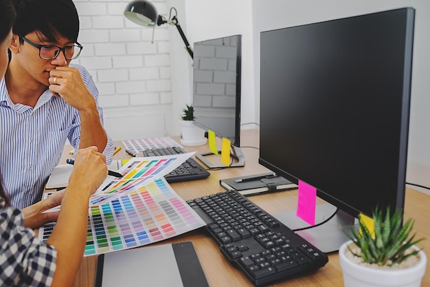 Geschäftsfrau, die mit einem Kollegen am Schreibtisch auf Farbproben zeigt.