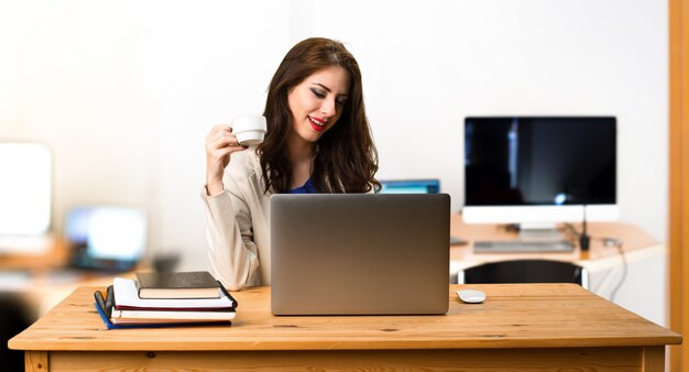 Geschäftsfrau, die mit ihrem Laptop arbeitet und einen Tasse Kaffee im Büro hält