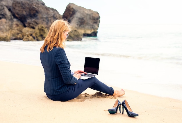 Geschäftsfrau, die mit Laptop-Computer am Strand arbeitet