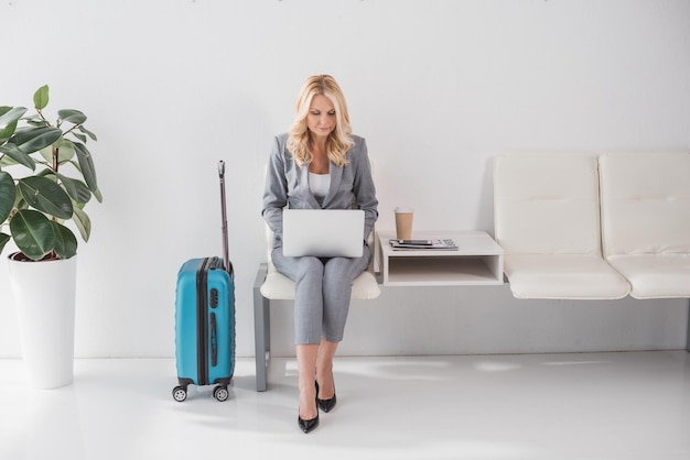 Geschäftsfrau, die mit Laptop in der Lobby arbeitet, während sie auf die Reise wartet