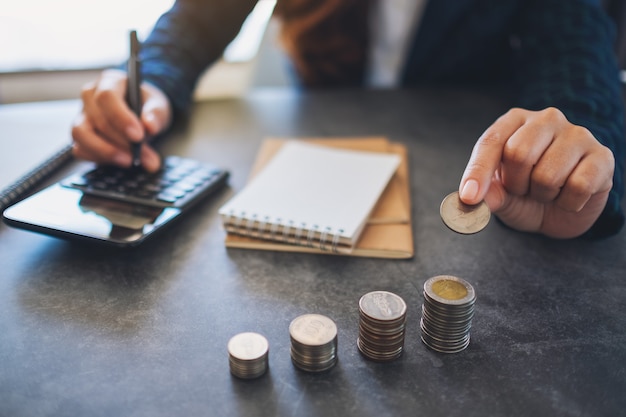 Geschäftsfrau, die Münzen hält und stapelt, während sie Geld auf dem Tisch berechnet