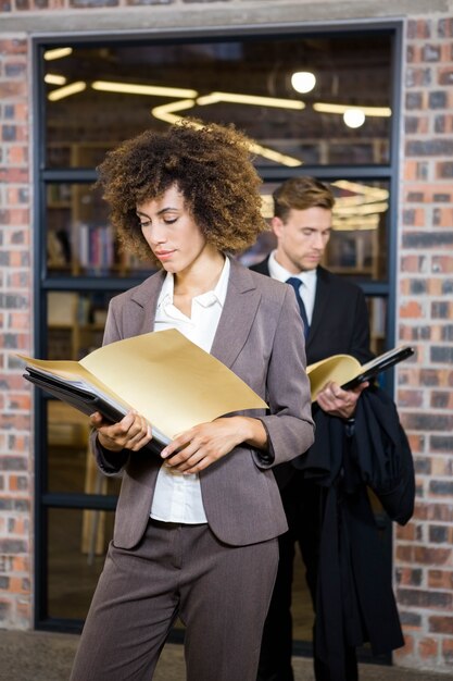 Geschäftsfrau, die nahe Bibliothek steht und Dokumente betrachtet