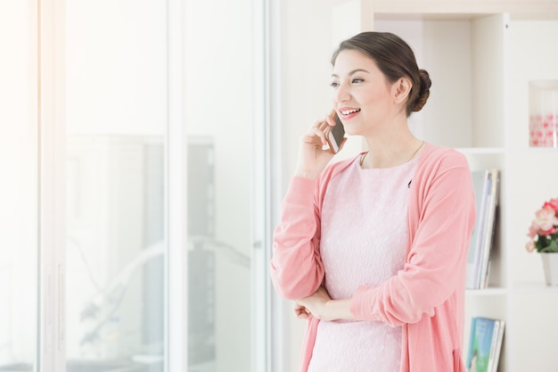 Geschäftsfrau, die nahe einem Fenster arbeiten und den Anruf telefonisch spricht im Büro hält.