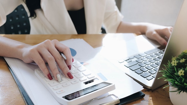 Geschäftsfrau, die Rechner und Laptop benutzt, um Mathefinanzierung auf hölzernem Schreibtisch im Büro zu tun.