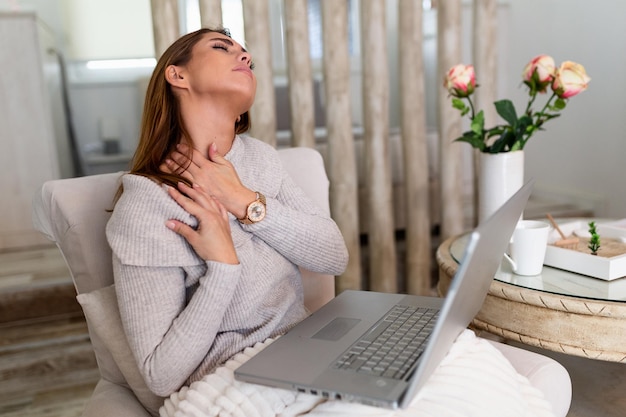 Geschäftsfrau, die Schmerzen im Nacken verspürt, nachdem sie mit Laptop am Tisch gesessen hat. Müde Frauen leiden unter Bürosyndrom wegen langer Computerarbeit. Hübsches Mädchen massiert ihre verspannten Nackenmuskeln