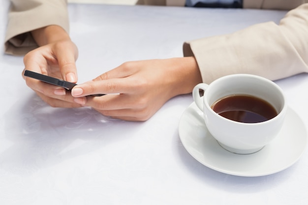 Geschäftsfrau, die Smartphone mit Kaffee verwendet