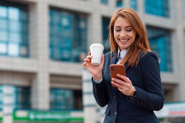 Geschäftsfrau, die Tasse Kaffee hodling und intelligentes Telefon verwendet