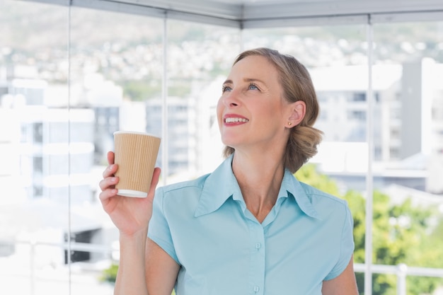 Geschäftsfrau, die Wegwerfkaffeetasse hält und oben schaut