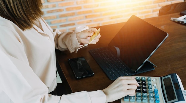 Geschäftsfrau hand verwendet Smartphone-Tablet-Zahlungen und hält Kreditkarten-Online-Shopping-Omni-Channel-Digital-Tablet-Docking-Tastatur-Computer im Büro im Sonnenlicht