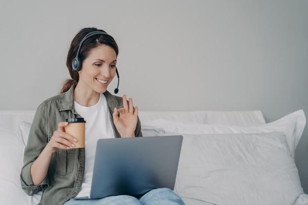 Geschäftsfrau im Headset-Gespräch per Videoanruf auf dem Laptop, wobei der Kunde eine Ok-Geste zeigt Remote-Job