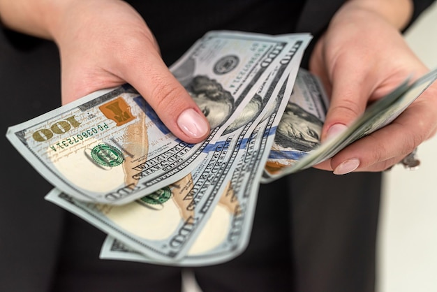 Geschäftsfrau in einem schwarzen klassischen Anzug hält ein paar neue Dollar in ihren schönen Händen