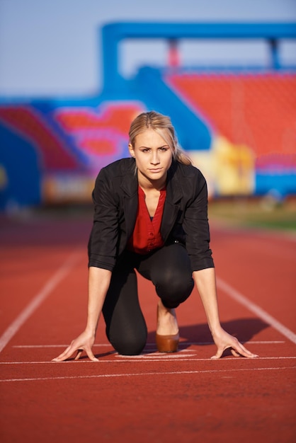 Geschäftsfrau in Startposition, bereit zum Laufen und Sprinten auf der Leichtathletik-Rennstrecke