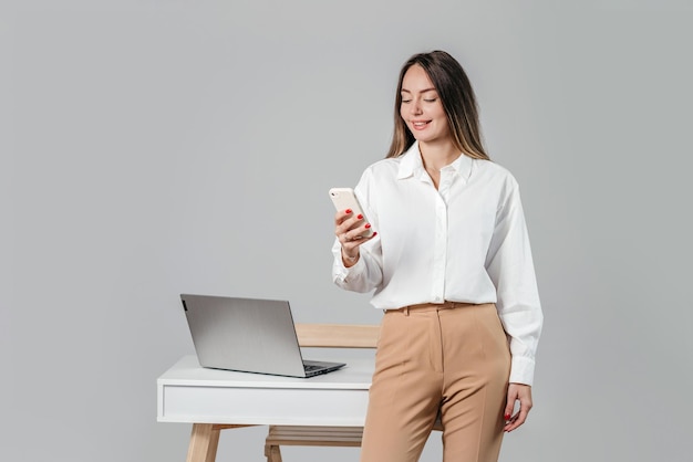 Geschäftsfrau lächelt und hält ein Mobiltelefon, isoliert auf grauem Hintergrund im Studio