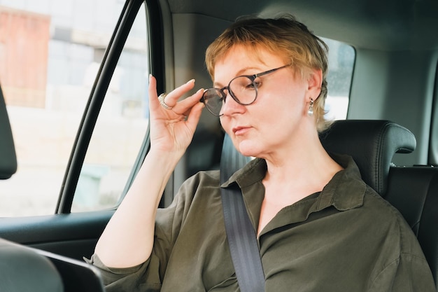 Geschäftsfrau mit Brille telefoniert, während sie auf dem Rücksitz eines Autos sitzt