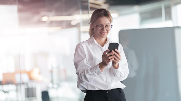 Geschäftsfrau mit Brille und Handy in der Hand im modernen Büro