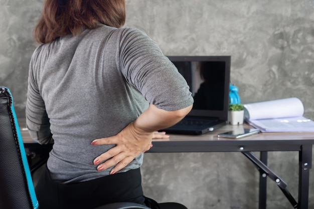 Foto geschäftsfrau mit büro-syndrom mit rückenschmerzen, die auf einem stuhl sitzt