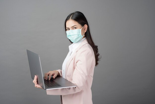 Geschäftsfrau mit der chirurgischen Maske hält Laptop-Computer