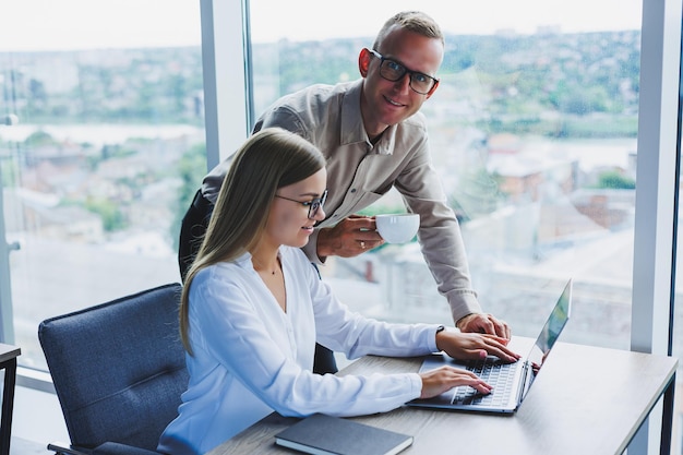 Geschäftsfrau mit einem Laptop für einen männlichen Kollegen, der in ein offenes Notizbuch schaut Geschäftliche Zusammenarbeit und Teamwork Europäische Millennials am Tisch im Büro Moderne erfolgreiche Menschen